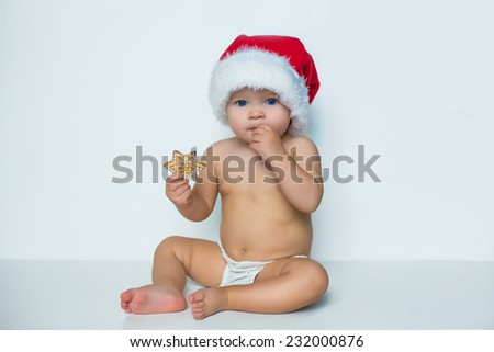 portrait of young infant adorable baby girl sitting on white in christmas hat and eating cookie