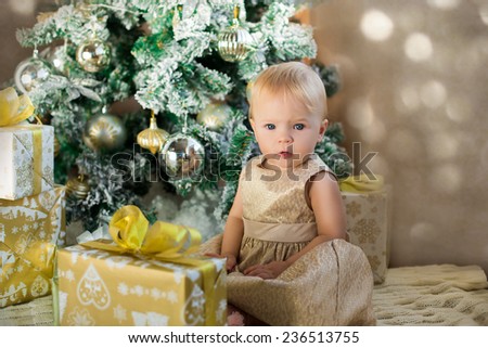 beautiful baby girl in golden dress unpacking presents under christmas tree