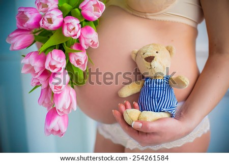 close up of pregnant belly. Spring inspiration with pink flowers tulips and teddy bear