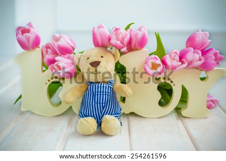 wooden letters baby background covered with spring flowers pink tulips and teddy bear on white floor