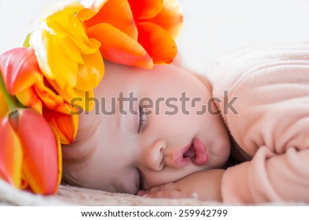 baby sleeping covered with spring flowers tulips