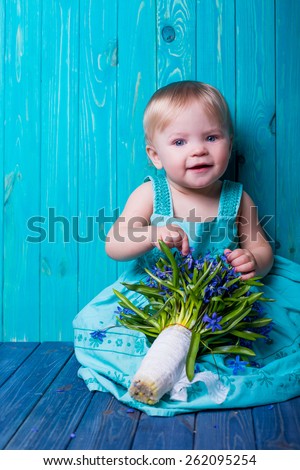 smiling emotional baby portrait summer style with bouquet of spring blue flowers on blue wooden background.