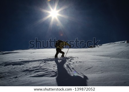The final summit push on skis to the mountain summit under the low winter sun in the alps.  Kicking in a new skin track in the fresh blowing snow.