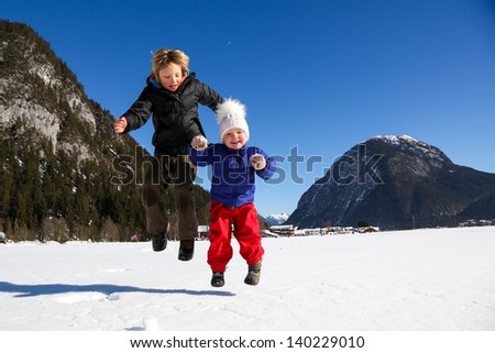 Brother and sister jumping high on a sunny winter day and having fun together.