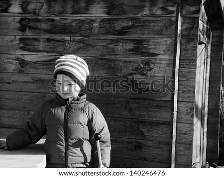 3 year old girl in winter sun by old shed.  Black and white.