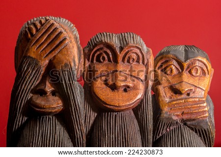 See hear speak no evil carved wooden monkeys on red background facing front