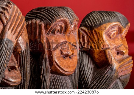 See hear speak no evil carved wooden monkeys on red background close up