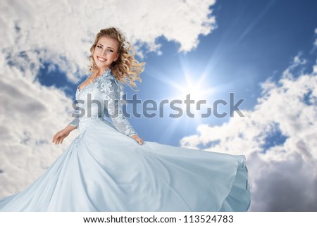Happy young bride in long beautiful dress against blue bright sunny sky