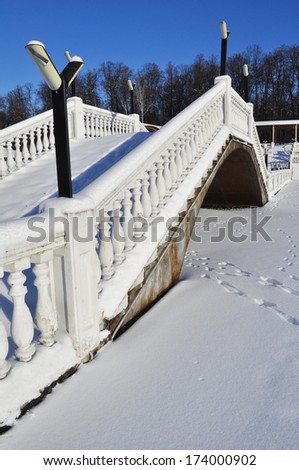 Snow-covered bridge railings through the frozen pond Sunny winter day.