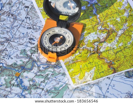 Compass in the black case on an orange ground open the mirror cover is located on a topographic map.