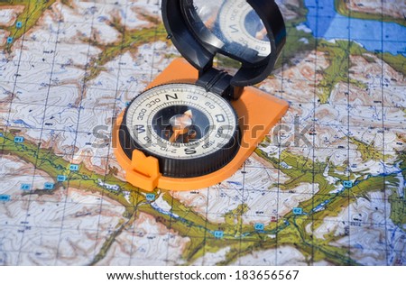 Compass in the black case on an orange ground open the mirror cover is located on a topographic map.
