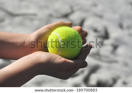 Yellow tennis ball, illuminated by the sun, in the hand of a child under the open sky.