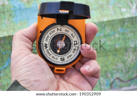 Magnetic compass in the black case on an orange ground with mirror cover to be in the hands of man.