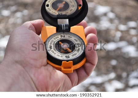 Magnetic compass in the black case on an orange ground with mirror cover to be in the hands of man.