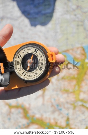 Open compass mirror cover in the palm of a man lying on the background of topographic maps.