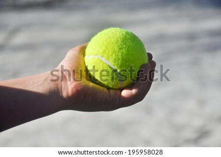 Tennis ball in his hand. The hand of the child squeezes yellow-green tennis ball against a light background.