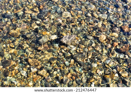 River pebbles under a thin layer of transparent water, illuminated by the sun.