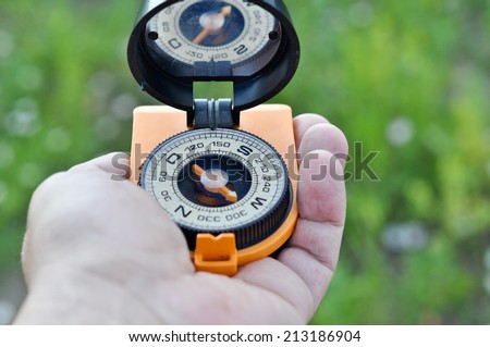 The compass in his hand. Magnetic compass in hand on the green meadows.