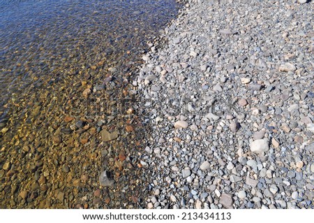 Background of river pebbles. River pebbles on the shore and under a thin layer of transparent water.