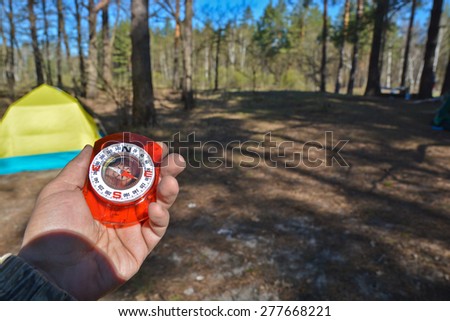 Compass and tourist tent. The magnetic compass in the hand against the tent in the forest in spring.