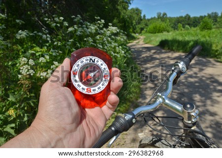 The compass and the bike. Magnetic compass in the hand and the handlebar on a background summer landscape.