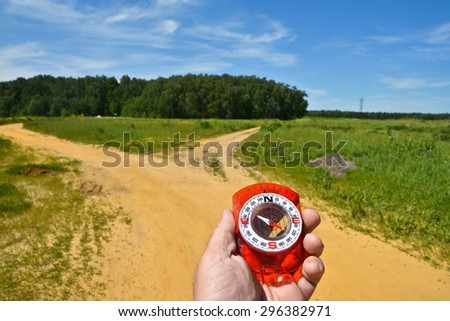 With the compass before the fork. The magnetic compass in the hand of a man to a fork in the road.
