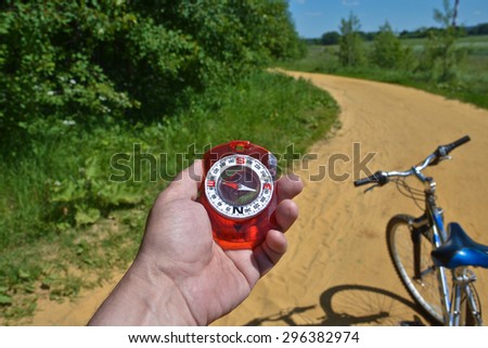 The compass and the bike. Magnetic compass in the hand and the handlebar on a background summer landscape.