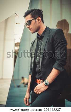 Man businessman in sunglasses posing near background of a mirror in architectural environment