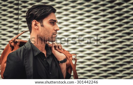 Stylish model looking man profile with handbag on his shoulder in modern architectural environment.