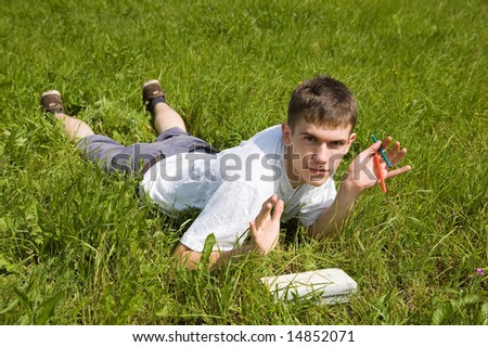 A young man reads a book, lying on a grass.