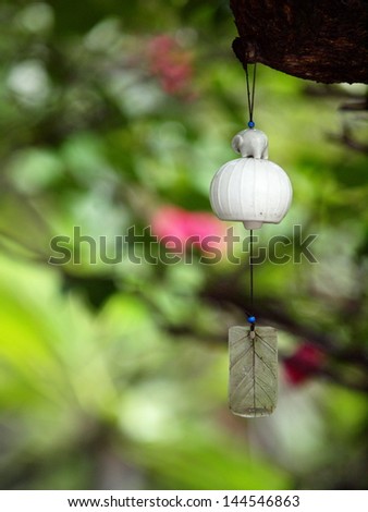 pearl white ceramic bell with elephant figure and sway leaf hanging in a garden