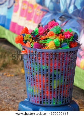 colorful plastic darts in basket for playing in typical dart game in vintage retro street festival in Thailand throwing at balloons to win for dolls and other prizes