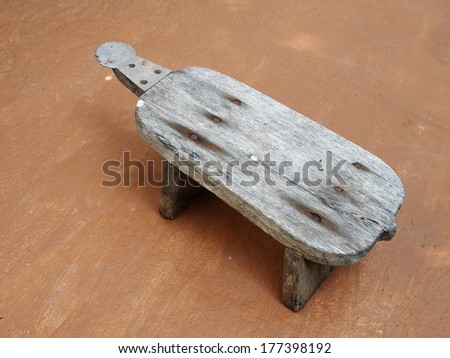 Thai old weathered retro vintage style wood coconut grater with sharp steel blade on a rough brown kitchen floor