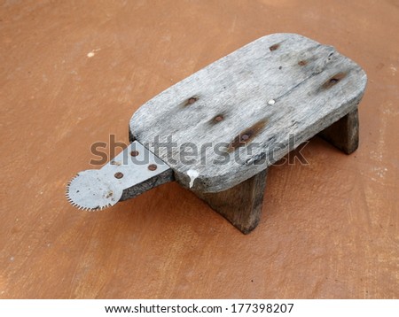 old weathered retro vintage style wood coconut grater with sharp steel blade on a rough brown kitchen floor