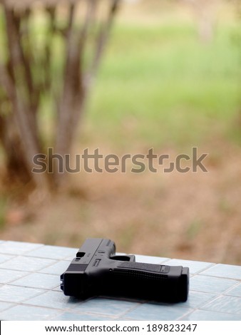 black air soft gun pistols model of a replica real pistol on an outdoor bench in green area in a garden of a country house
