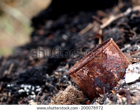 dark ash and rest of burned toxic waste such as plastic metal and daily used chemical as human-made surrounding pollution environment leaving on the ground and water in nature for the next generation
