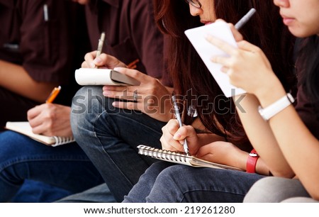 unidentified young asian female student school girls wearing jeans sitting on the floor outdoor taking note at site visit on small paper notebook with pen and pencil