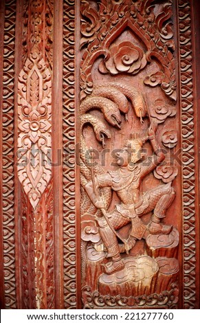 hand crafted work of THAI artist on a red brown hardwood temple door plate showing typical traditional pattern ornaments, tree, human, animals and god figures for buddhism temple decoration