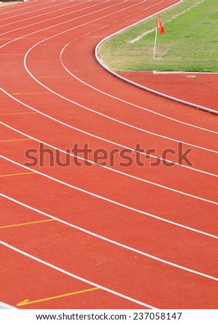 red race running track rough texture white curve lines in the corner of a green grass sport field with a small red flag