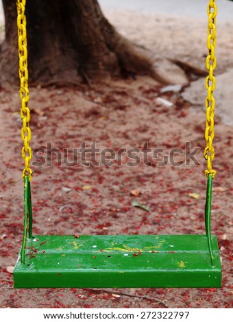 metal swing for children on outdoor playground in a kindergarten made of iron plate chain and rod painted in colorful green color hanging outdoor in backyard garden under evening sunlight and shadow