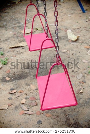 metal swing for children on outdoor playground in a kindergarten made of iron plate chain and rod painted in colorful red color hanging outdoor in backyard garden under evening sunlight and shadow