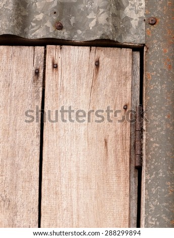 old aged abandoned weathered wood surface of a gray color old country house door with rusty metal door fittings installed