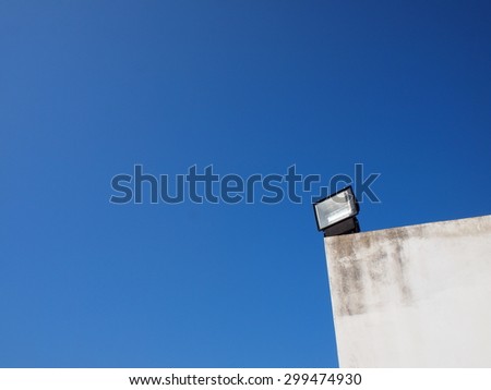 black body metal outdoor flood light lamp with chrome reflection inside installed on an old white building isolated with deep clear blue sky background