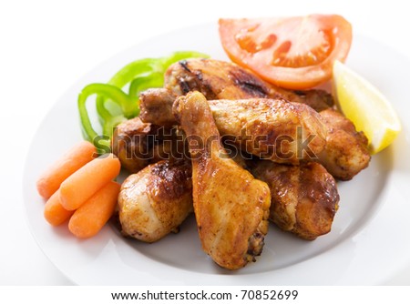 Roasted chicken drumsticks on white plate with lemon and tomato