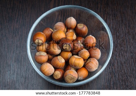 Brown fisful of hazelnuts in the shell in glass transparent dish on dark wooden background