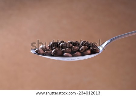 Steel spoon of roasted coffee beans on light brown background