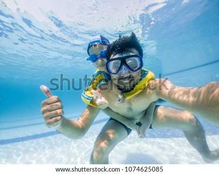 Happy young asian kid and dad with swim goggles underwater, smile relax face swimmer have fun activity