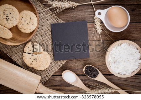 Rural vintage wooden kitchen table with old blank sheet of paper, baking cookie ingredients and cooking utensils around. Background with free recipe text space.