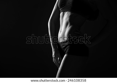 Athletic young woman with beautiful abdominal muscles on dark background. black and whites photo