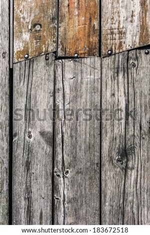Very old, weathered, rotten floorboards, fixed and patched with planks of different origin, with uneven in-between gaps, large wood knots, and round head machine screws embedded - detail.